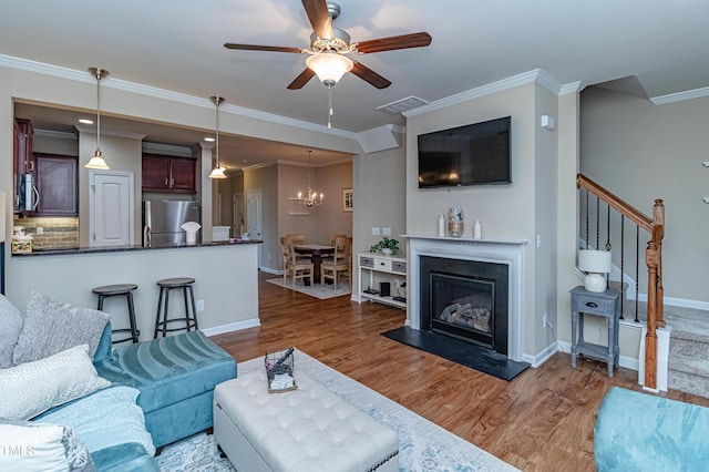 living area with visible vents, baseboards, stairs, ceiling fan with notable chandelier, and wood finished floors