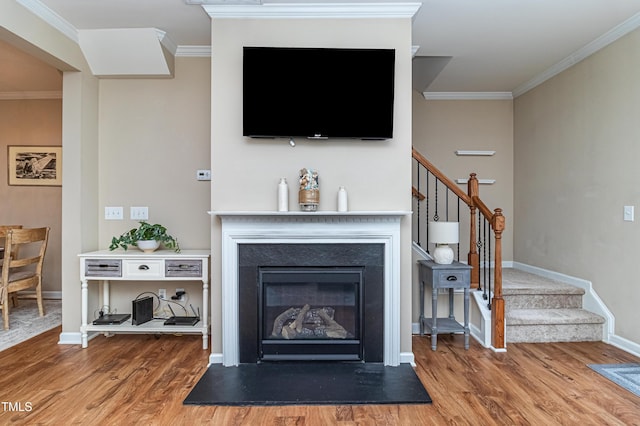 living room featuring a glass covered fireplace, crown molding, stairs, and wood finished floors