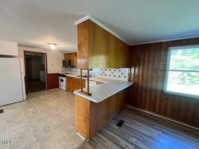 167 Chic Ennis Rd, Coats, NC 27521 - kitchen featuring a peninsula, brown cabinetry, white appliances, wood walls, and light countertops