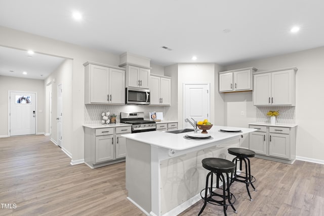 kitchen featuring stainless steel appliances, a sink, visible vents, light wood finished floors, and a center island with sink