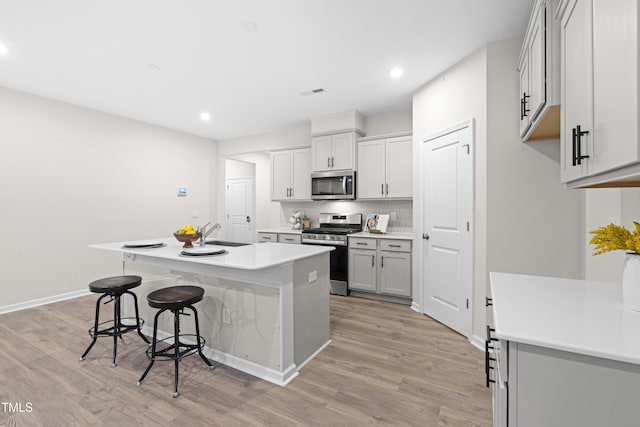 kitchen featuring light wood-style flooring, stainless steel appliances, a breakfast bar, a sink, and a center island with sink