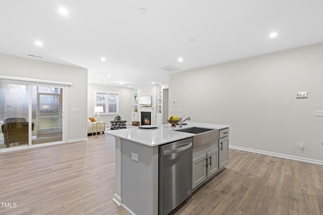 kitchen featuring gray cabinetry, light wood-style floors, a sink, dishwasher, and a lit fireplace