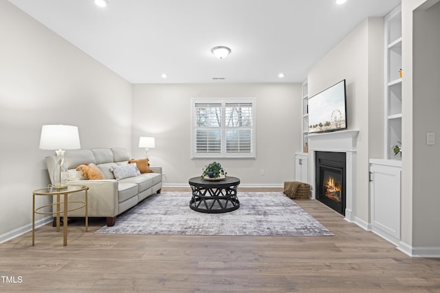 living room with a glass covered fireplace, baseboards, and wood finished floors