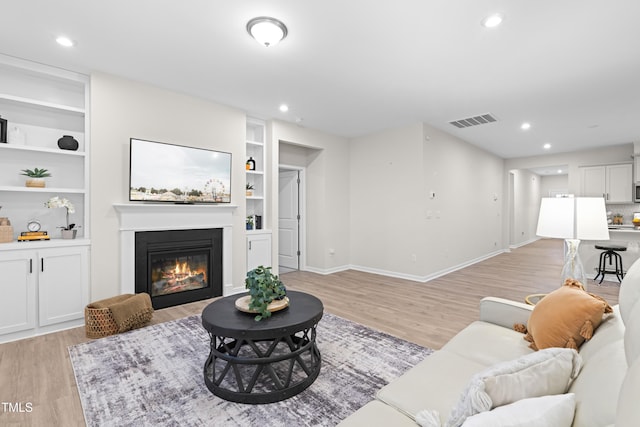 living area with recessed lighting, visible vents, baseboards, light wood-style floors, and a glass covered fireplace