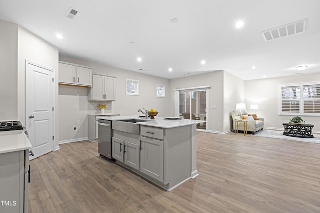 kitchen with open floor plan, stainless steel dishwasher, light wood-type flooring, and visible vents