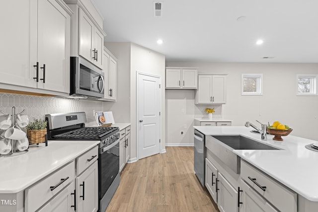 kitchen with decorative backsplash, appliances with stainless steel finishes, light countertops, light wood-style floors, and a sink