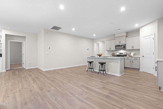 kitchen with a center island with sink, visible vents, light wood-style flooring, appliances with stainless steel finishes, and recessed lighting