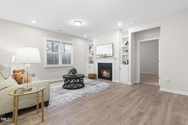 living area featuring a glass covered fireplace, recessed lighting, wood finished floors, and baseboards