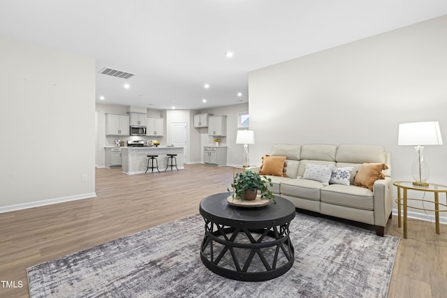 living area with recessed lighting, baseboards, visible vents, and light wood finished floors