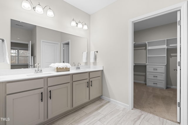 full bath featuring a spacious closet, double vanity, a sink, and baseboards