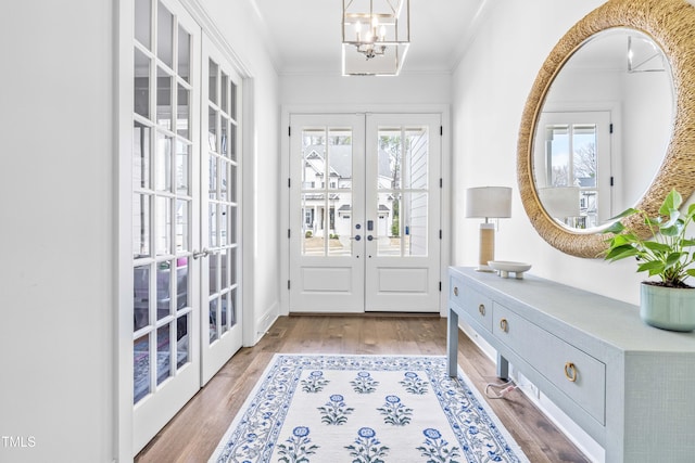 foyer entrance with a notable chandelier, french doors, crown molding, and wood finished floors