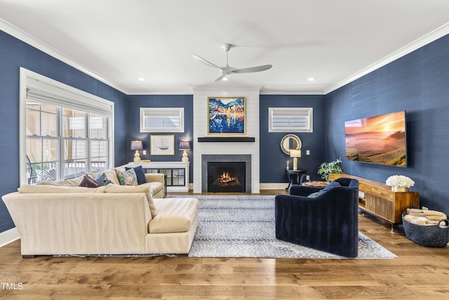 living area with a ceiling fan, wood finished floors, baseboards, ornamental molding, and a large fireplace