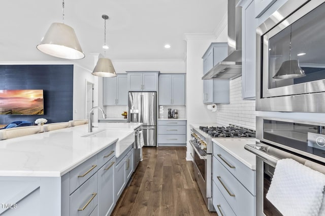 kitchen with gray cabinets, a sink, appliances with stainless steel finishes, decorative light fixtures, and wall chimney exhaust hood