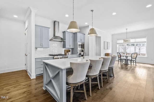 kitchen with tasteful backsplash, wall chimney range hood, a center island with sink, light countertops, and gray cabinets