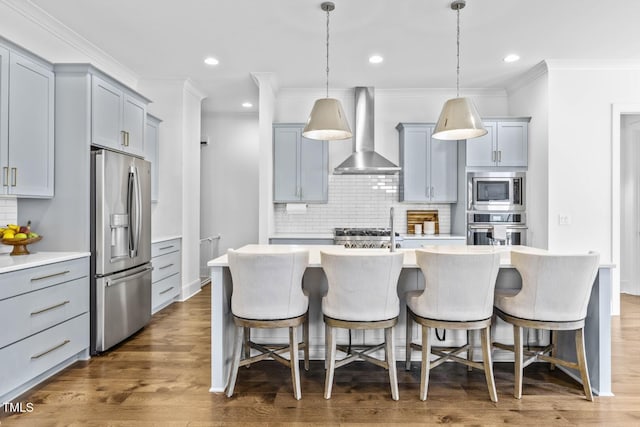 kitchen featuring a breakfast bar area, light countertops, wood finished floors, stainless steel appliances, and wall chimney exhaust hood