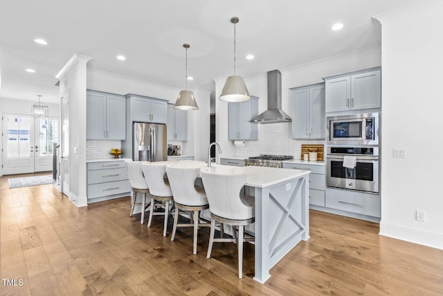 kitchen with wall chimney range hood, light countertops, a kitchen bar, gray cabinets, and appliances with stainless steel finishes