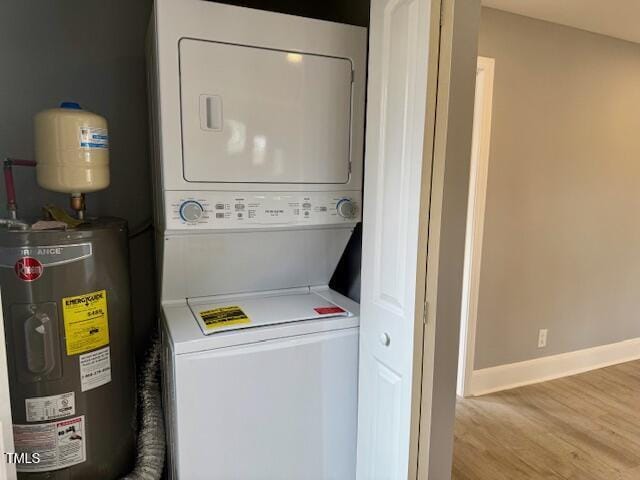 washroom with electric water heater, wood finished floors, stacked washer / dryer, baseboards, and laundry area