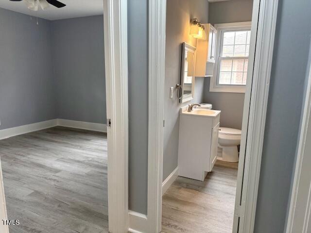 half bath with vanity, toilet, wood finished floors, and baseboards