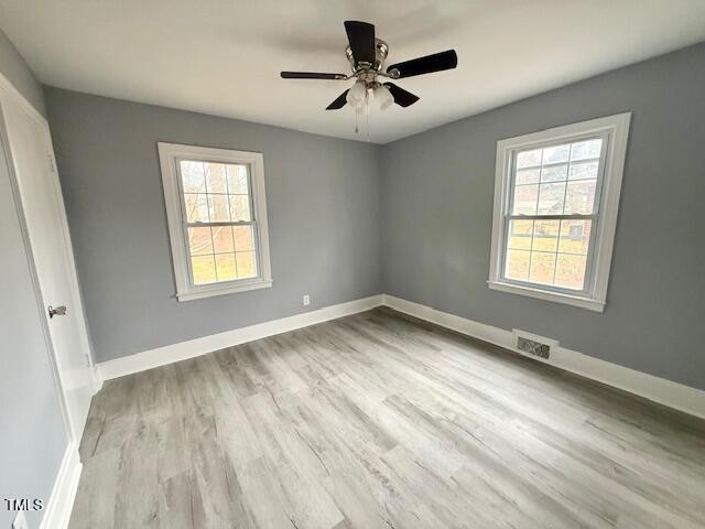 spare room with wood finished floors, plenty of natural light, baseboards, and visible vents