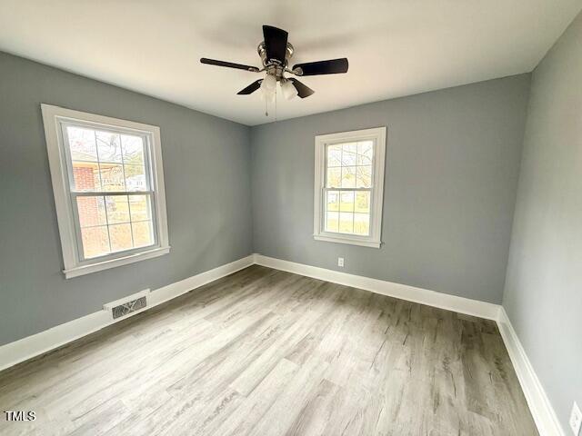 empty room featuring visible vents, a ceiling fan, baseboards, and wood finished floors