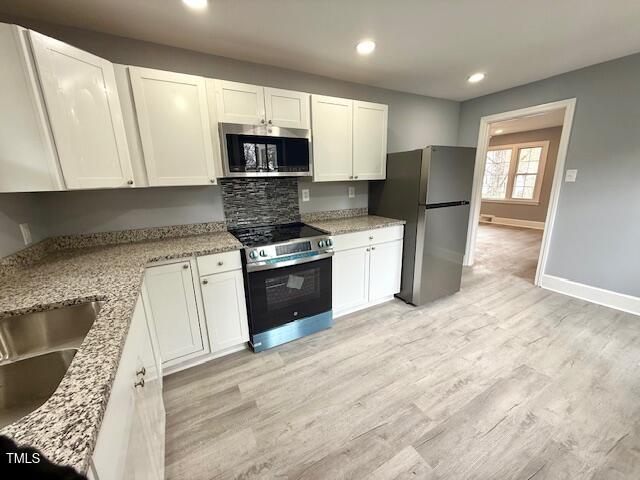 kitchen with light stone counters, baseboards, light wood-style flooring, appliances with stainless steel finishes, and white cabinetry