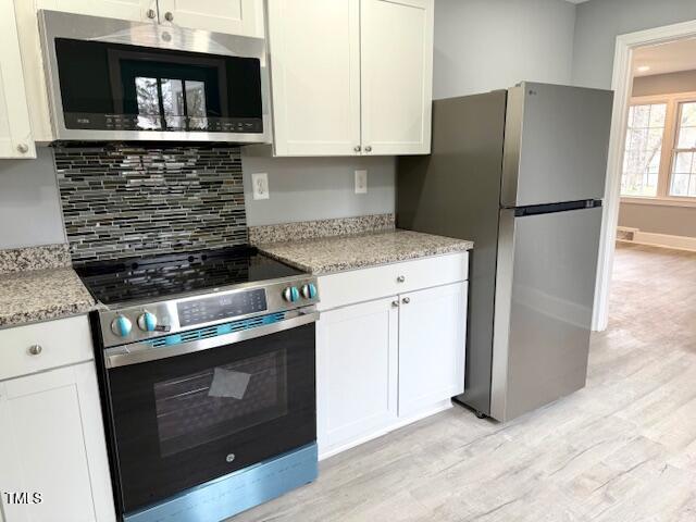 kitchen featuring light stone counters, light wood-style flooring, appliances with stainless steel finishes, white cabinetry, and tasteful backsplash