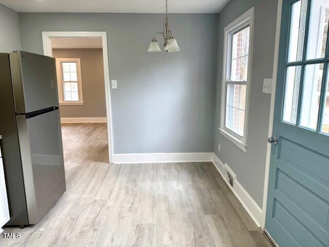 unfurnished dining area with a wealth of natural light, light wood-type flooring, and a notable chandelier