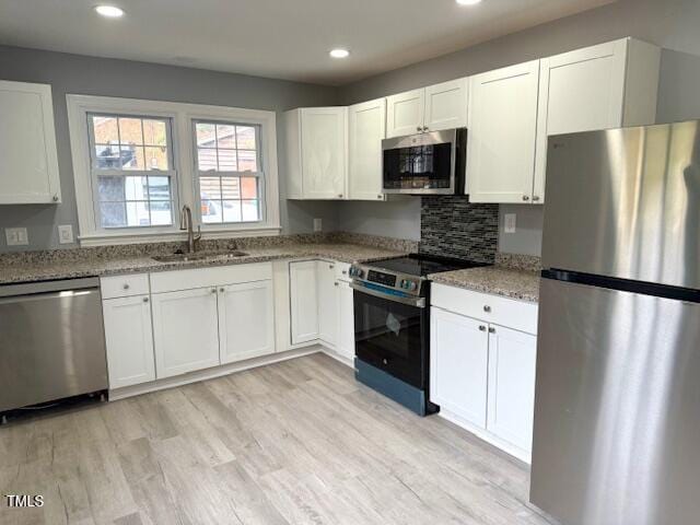 kitchen with light stone countertops, light wood-type flooring, stainless steel appliances, white cabinetry, and a sink