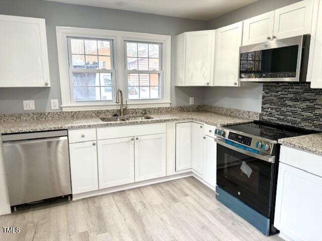 kitchen featuring light wood-style flooring, a sink, backsplash, white cabinetry, and stainless steel appliances