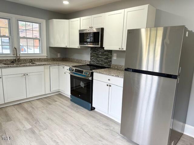 kitchen with light wood-style flooring, a sink, stainless steel appliances, white cabinets, and light stone countertops