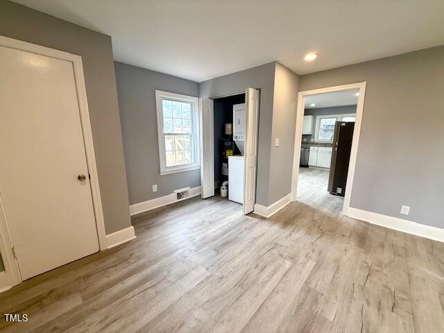 unfurnished bedroom featuring baseboards, light wood-type flooring, and freestanding refrigerator