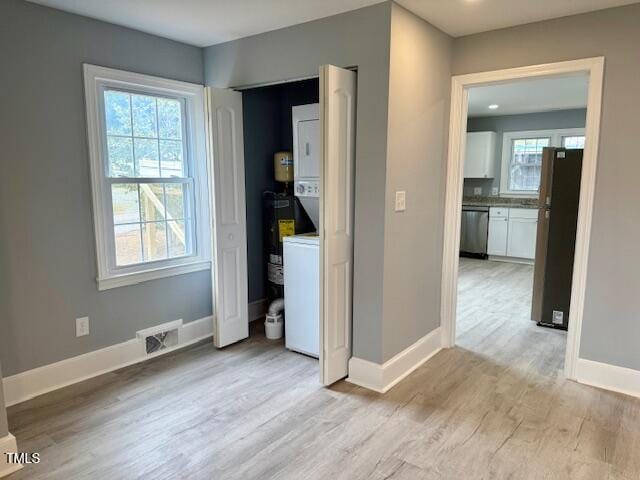 unfurnished bedroom featuring visible vents, baseboards, light wood-type flooring, freestanding refrigerator, and stacked washer / drying machine