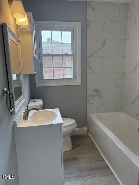 bathroom with toilet, shower / washtub combination, wood finished floors, baseboards, and vanity