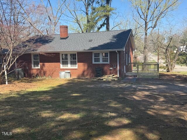 exterior space with a lawn, a chimney, a shingled roof, and brick siding