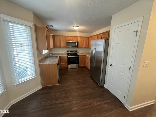 kitchen with dark wood-style flooring, light countertops, appliances with stainless steel finishes, a sink, and baseboards