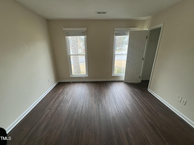 unfurnished room featuring a healthy amount of sunlight, visible vents, baseboards, and dark wood-style flooring