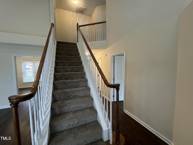 staircase with a high ceiling, visible vents, baseboards, and wood finished floors