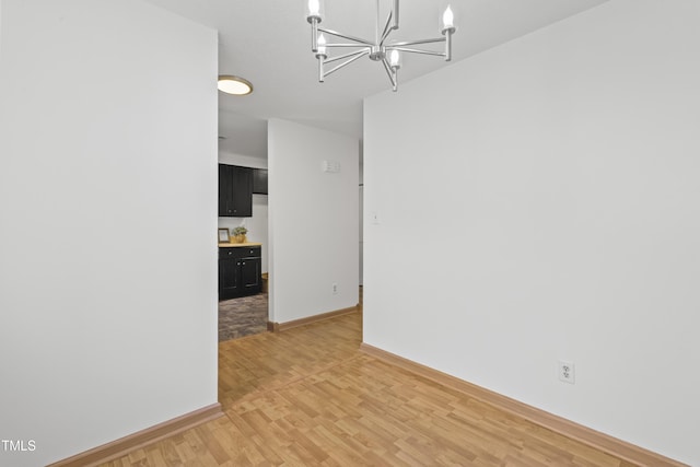 unfurnished dining area with baseboards, an inviting chandelier, and light wood-style floors