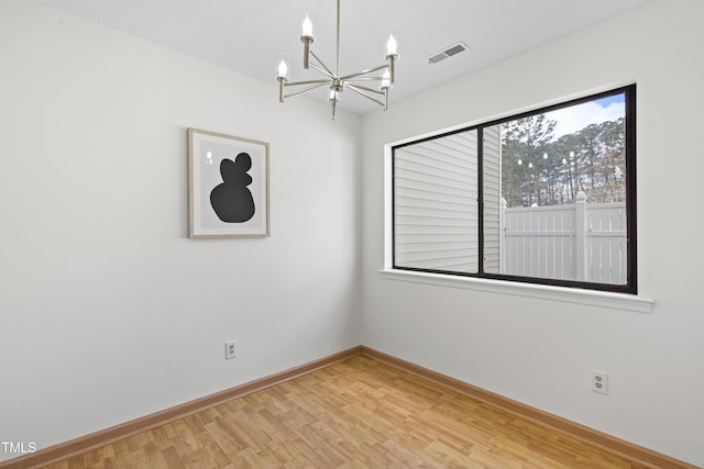 empty room featuring a chandelier, wood finished floors, visible vents, and baseboards