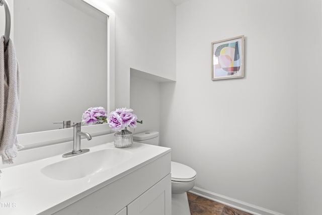 bathroom featuring toilet, stone finish flooring, baseboards, and vanity