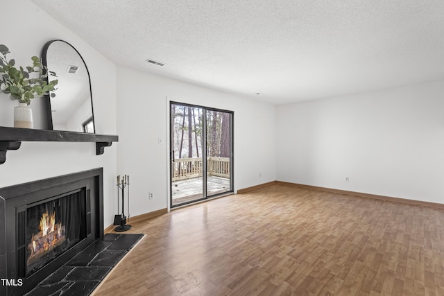 unfurnished living room with baseboards, a lit fireplace, a textured ceiling, and wood finished floors