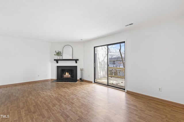 unfurnished living room featuring a lit fireplace, wood finished floors, visible vents, and baseboards