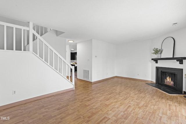 unfurnished living room with stairway, a lit fireplace, visible vents, and wood finished floors