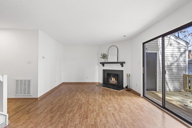 unfurnished living room featuring a lit fireplace, light wood finished floors, visible vents, and baseboards