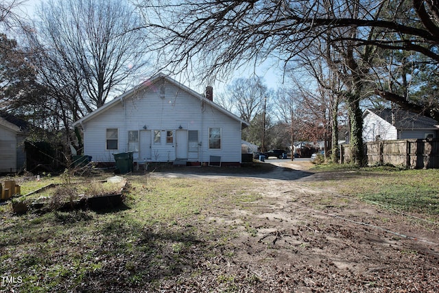 view of side of property featuring dirt driveway, a chimney, and fence