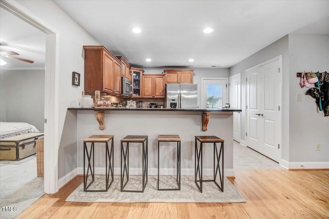 kitchen featuring dark countertops, glass insert cabinets, appliances with stainless steel finishes, a kitchen breakfast bar, and a peninsula