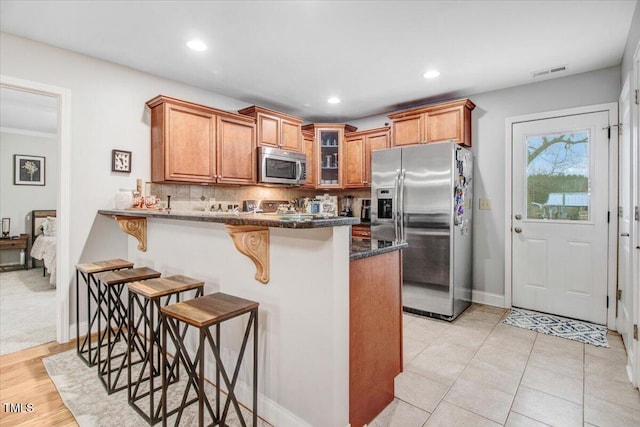 kitchen with visible vents, a breakfast bar area, appliances with stainless steel finishes, glass insert cabinets, and a peninsula