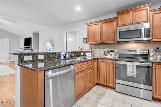 kitchen with appliances with stainless steel finishes, brown cabinets, a sink, and a peninsula