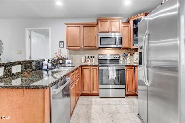 kitchen featuring brown cabinetry, dark stone counters, a peninsula, stainless steel appliances, and a sink