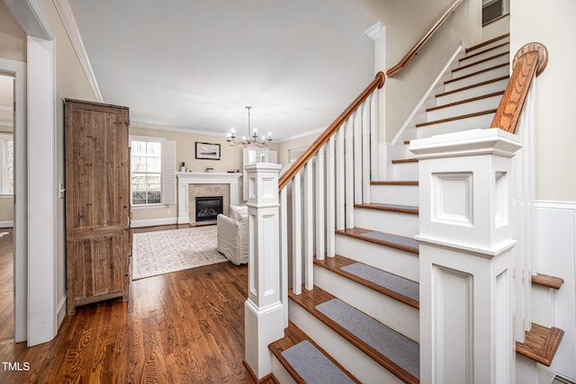 stairway featuring ornamental molding, a glass covered fireplace, an inviting chandelier, and wood finished floors